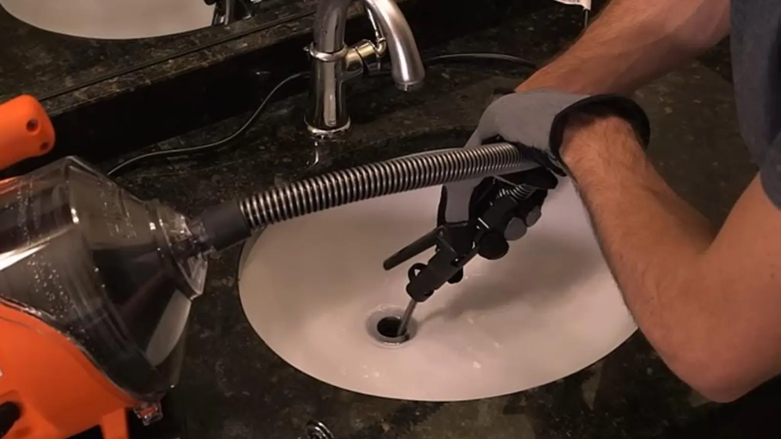 Plumber working a drain snake cable into a bathroom sink drain