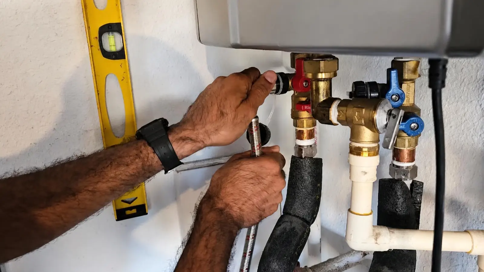 Hands working on the service valves under a wall-mounted tankless water heater