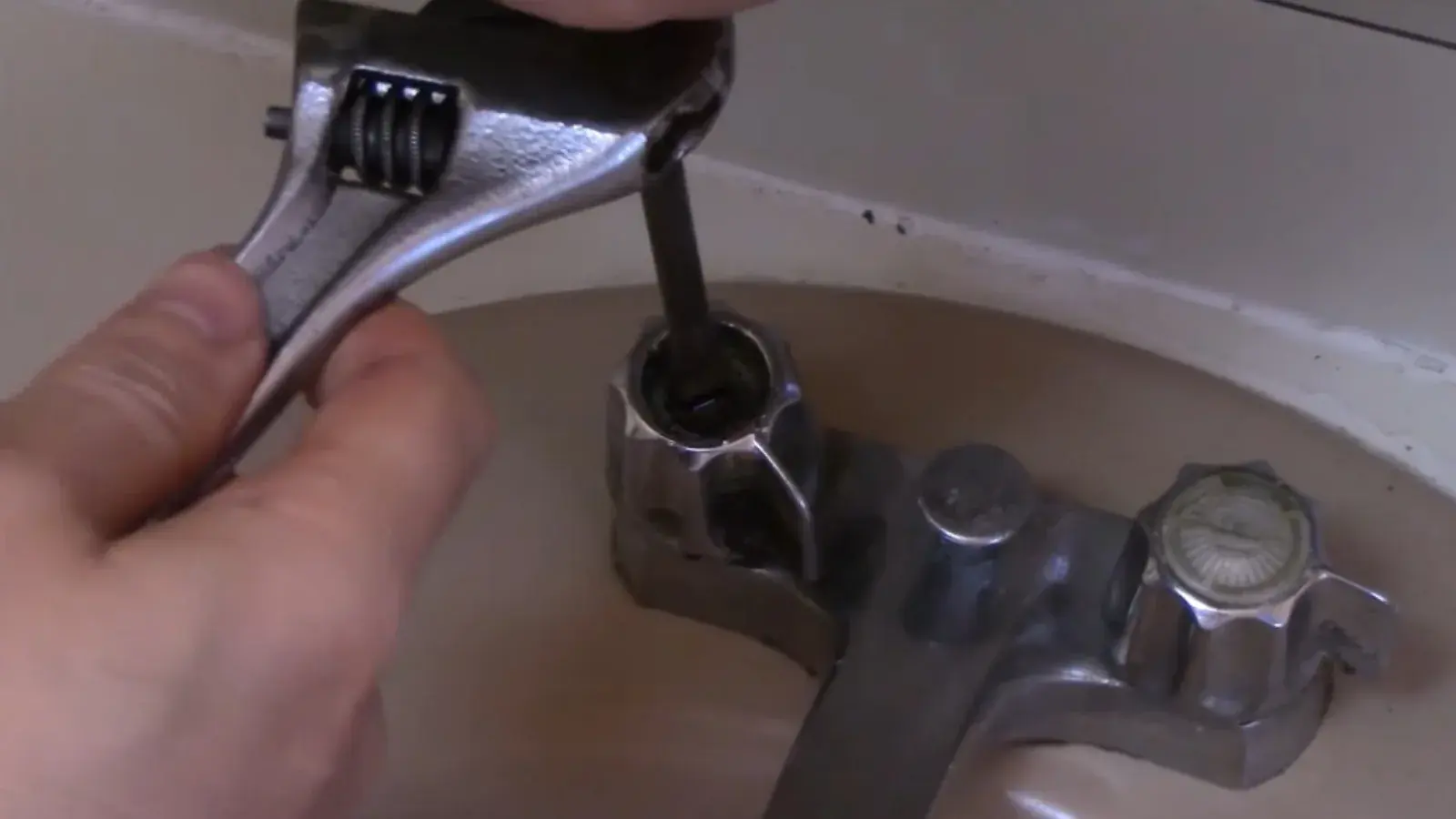 Hand using an adjustable wrench on an older two-handle tub faucet
