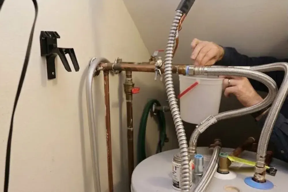 Plumber working on the flexible supply lines and fittings at the top of a tank water heater